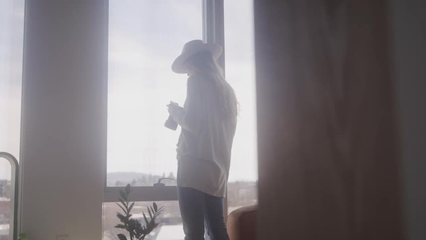 A woman is looking out the window at home