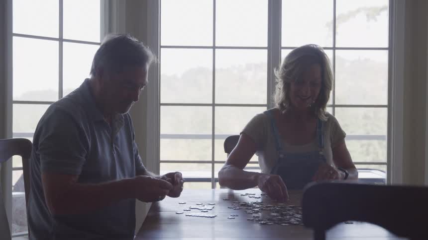 Happy couple laughing and chatting sitting at dining table building a puzzle