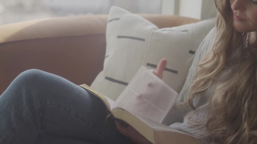 Woman with long hair relaxing on couch reading a book