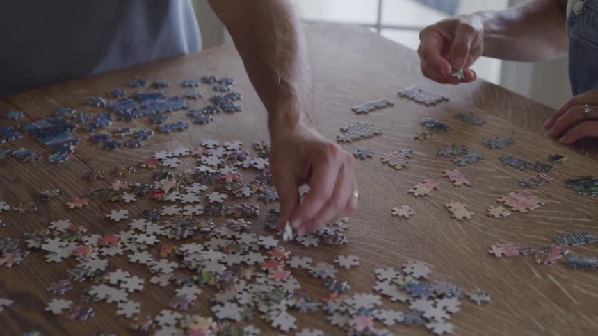 Close up of couple building a puzzle on dining table