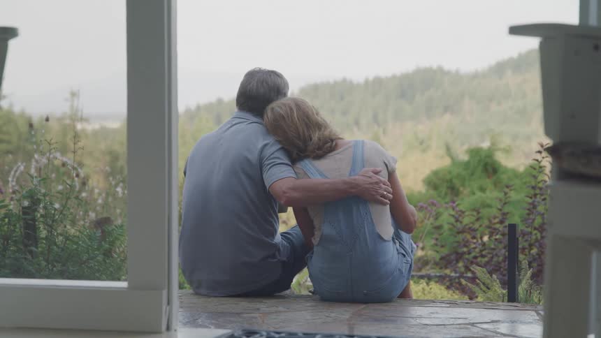 A husband and wife sitting on the steps enjoying the view in front of their house