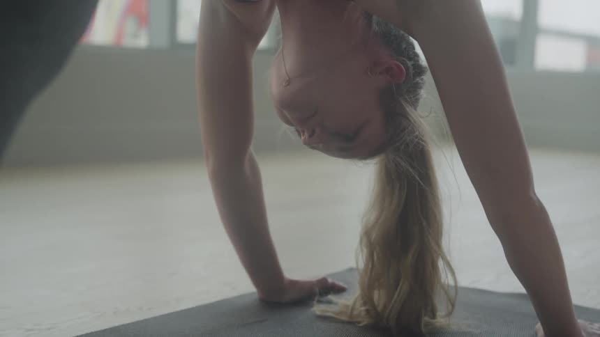 Inside an empty gym a woman is doing a yoga pose