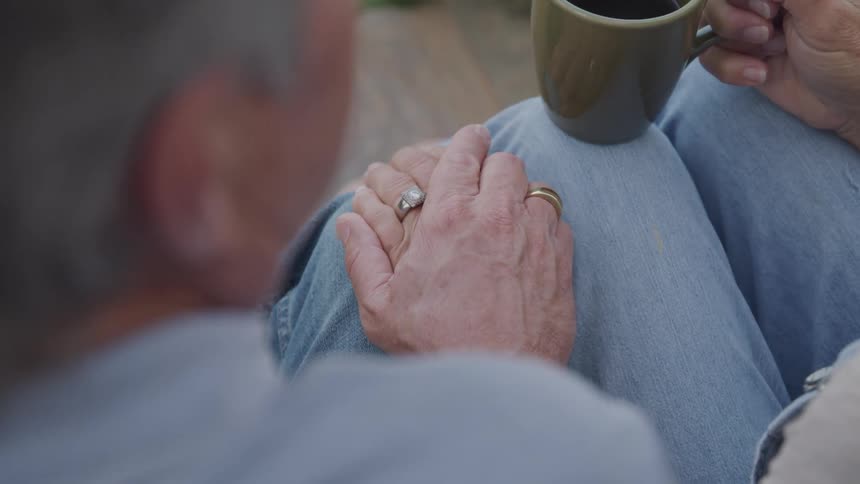 An elderly couple shares a quiet moment holding hands and enjoying a cup of coffee together