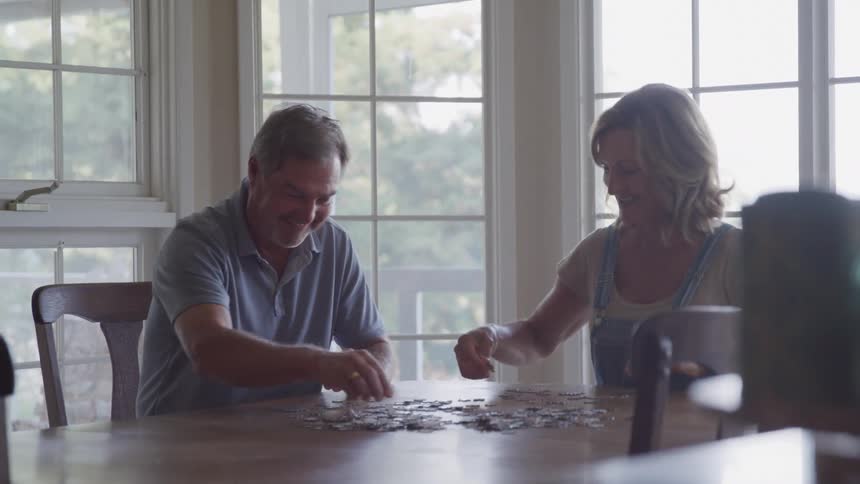 Happy couple laughing and chatting building a puzzle on dining table