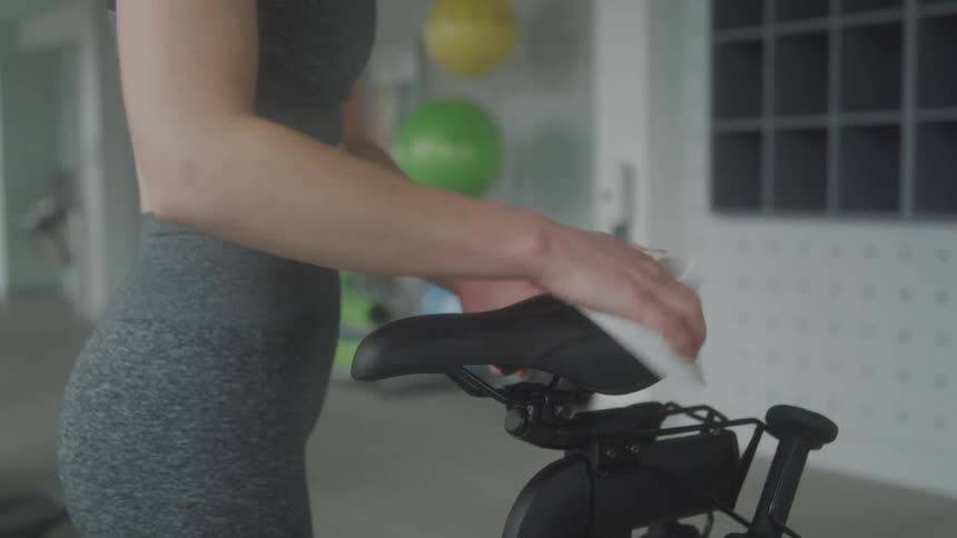 A woman cleans the seat on the exercise bike