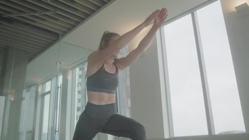 Blonde woman moves from one yoga pose into another while working out during the daytime