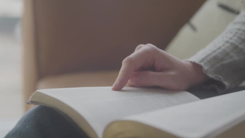 The camera zooms in on a feminine finger tracing along a passage on a bible resting on her knees inside a quiet room