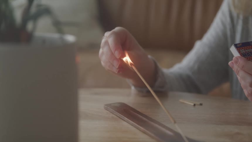 Woman sitting at round table lighting an incense off a metal stand