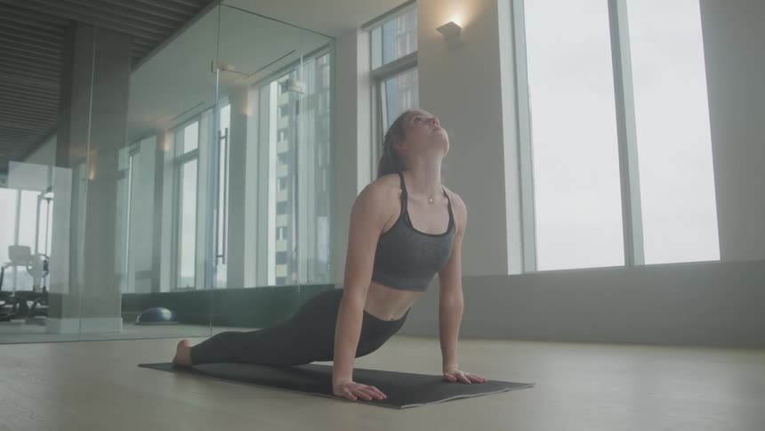 Inside a well lit gym a woman is doing yoga by herself