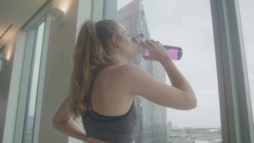 A woman is looking out the window and drinking water