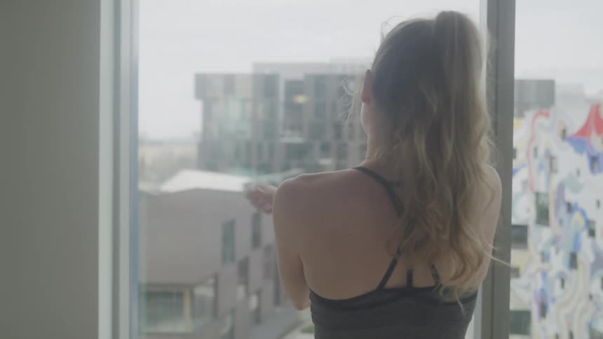 A woman stretches contently by a window overlooking a cityscape