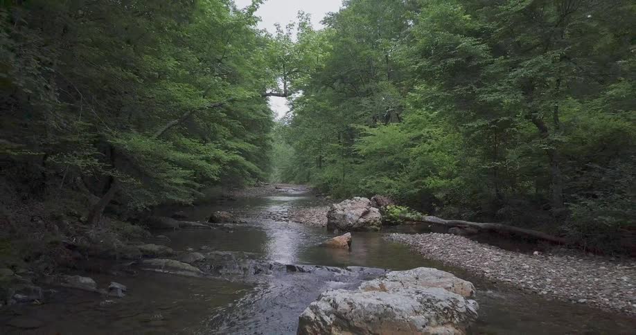 Aerial view moving down a small river with large rocks in it