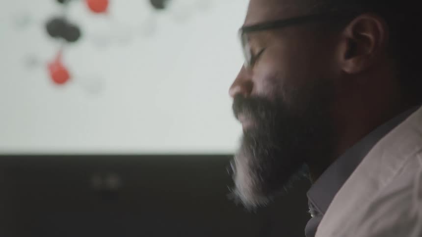 A thinking man sits in an office with a large monitor next to him showing a mind map