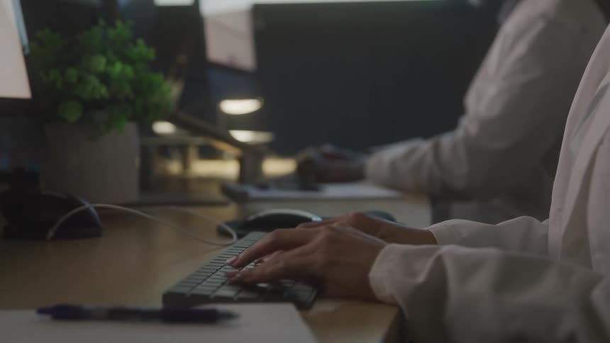 Closeup of hands typing on a keyboard at a computer desk in a dimly lit office