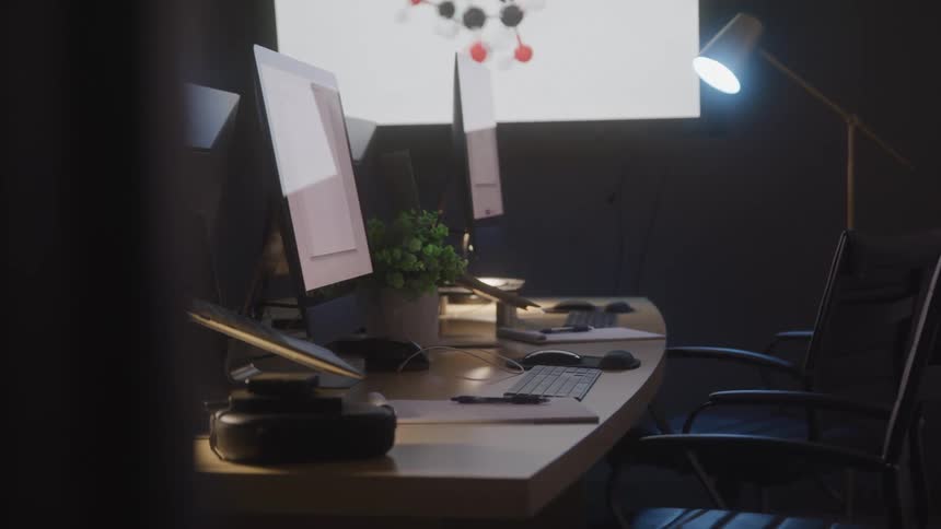 A dimly lit workspace features multiple computer monitors a keyboard a mouse a potted plant a vr headset and a desk lamp illuminating the scene