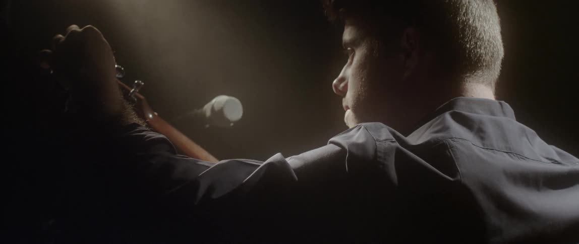 A man is examining some equipment and his guitar in a dark room
