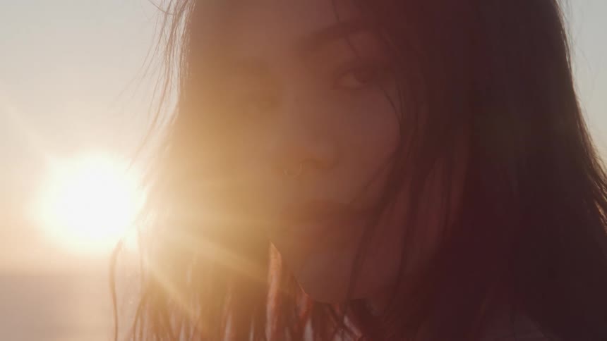 A young woman is looking forward with the sky and bright sun behind her