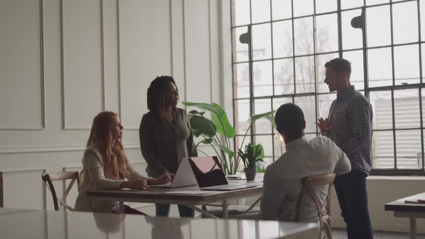 Four individuals are gathered around a table in a bright office engaged in a discussion