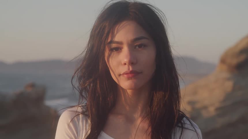 Woman standing outdoors near a hill turns her head to stare