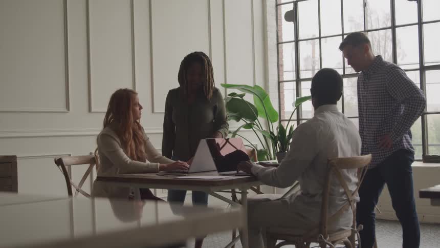 A group of professionals collaborates around a laptop in a modern office