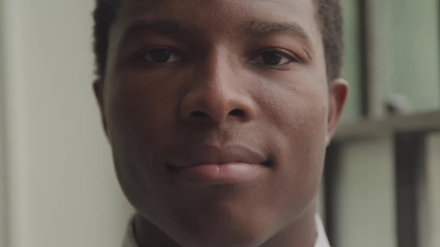 The face of a young man with short dark hair looking directly at the camera with a neutral expression