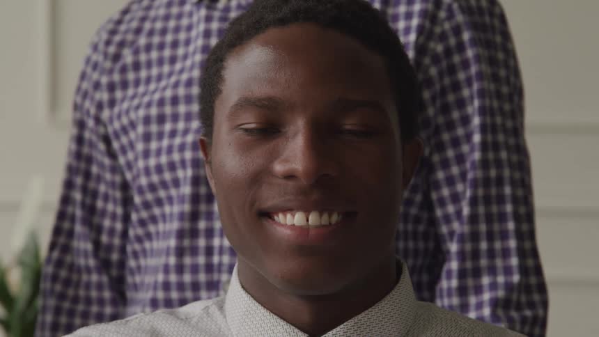 Smiling black man sitting in front of person in plaid shirtblinking his eyes