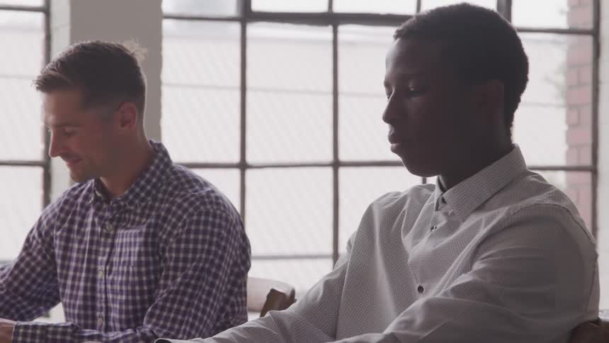 A man nods to a coworker at his desk