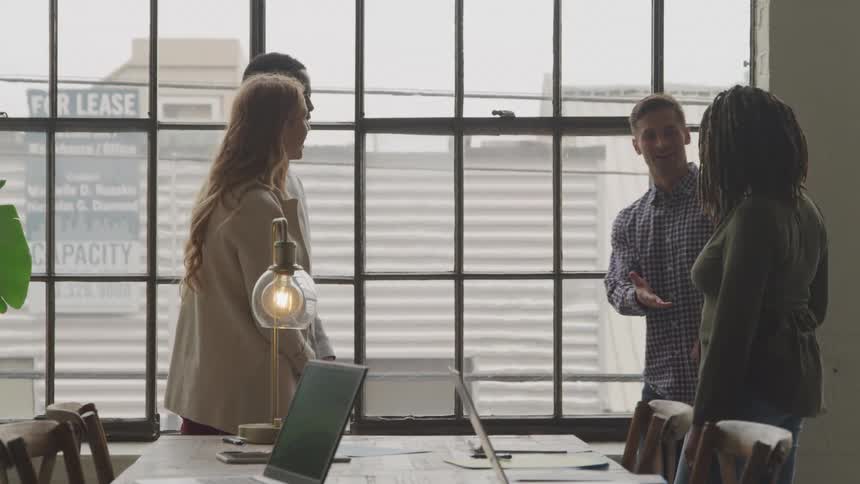 Office workers shake hands with clients while standing in a meeting room during the day