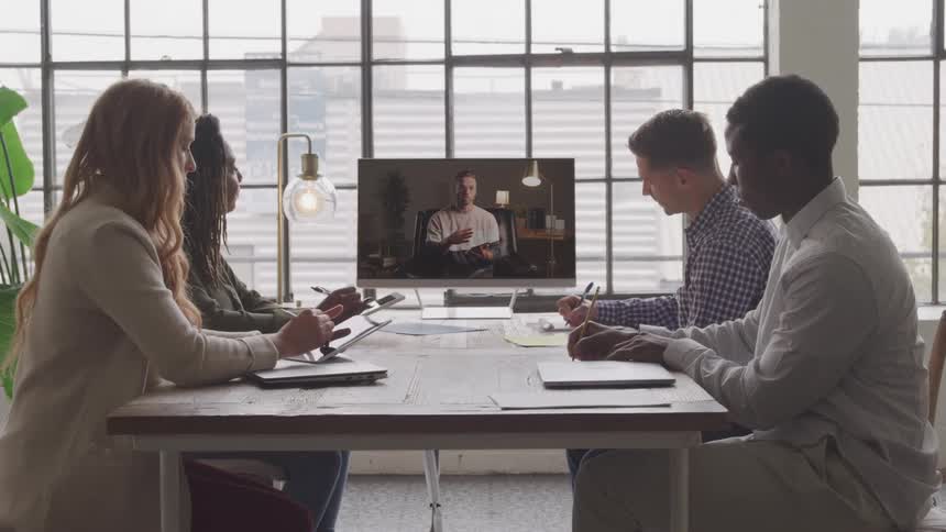 Workers are listening to a man on the screen at a meeting