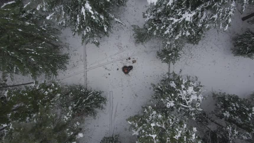 A person is sitting by the campfire in the forest filled with snow