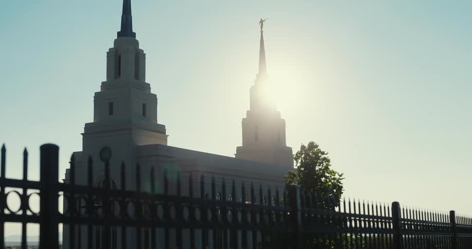 The layton utah temple stands silhouetted against a bright clear sky framed by a dark ornate fence in the foreground