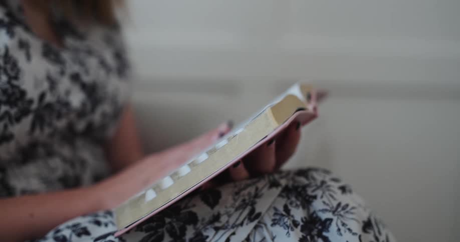 Woman wearing black and white floral dress sitting in a room reading a book