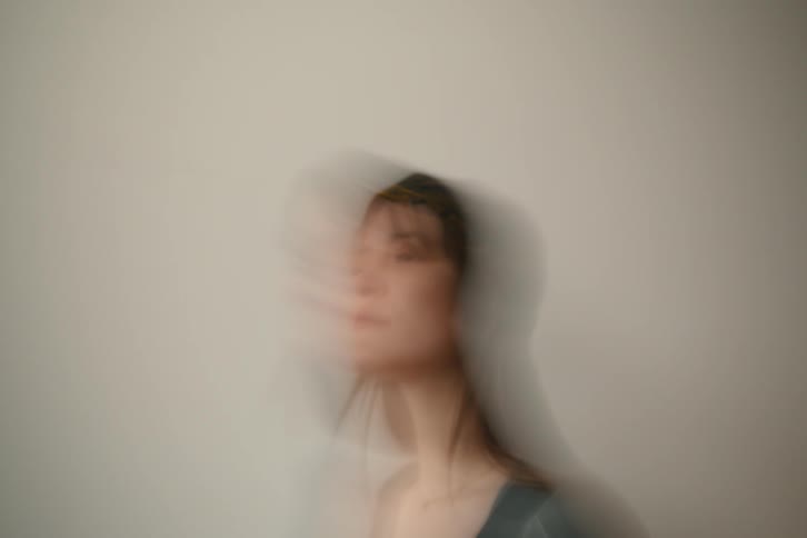 A woman with dark hair and a yellow headband is captured against a light background