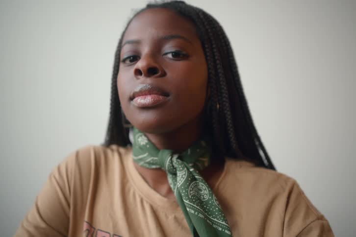 A black woman with long braids is shown from the chest up wearing a bandanna around her neck
