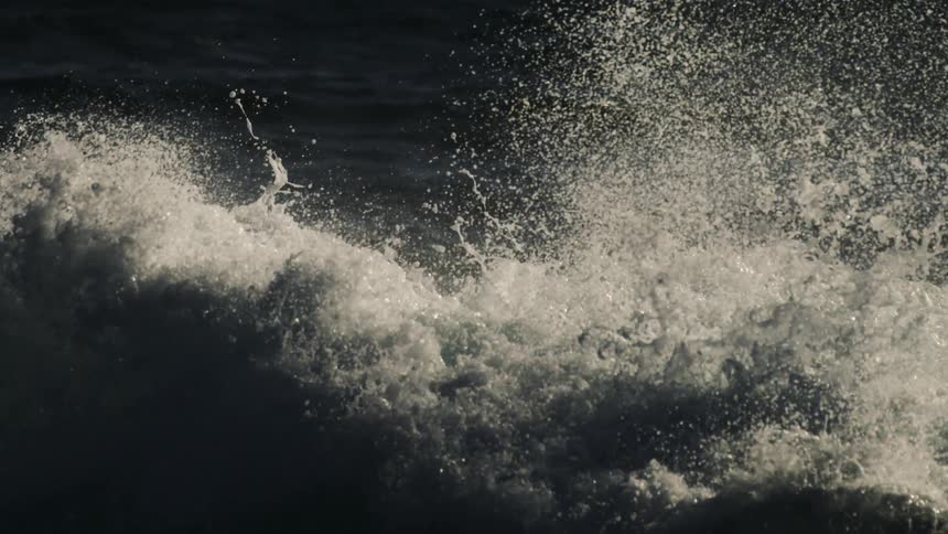 The dynamic texture of white sea spray against the dark shadowy surface of the ocean