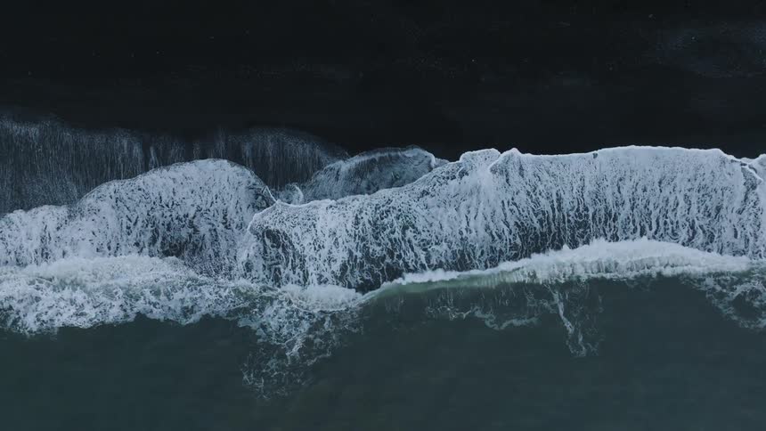Birds eye view of waves crashing onto a black sand shoreline