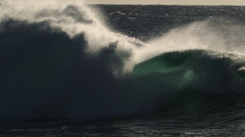 In a timelapsed capture an ocean wave breaks across the ocean spraying plumes of white mist and spray in the air as the waves become huge and then smash back into the ocean