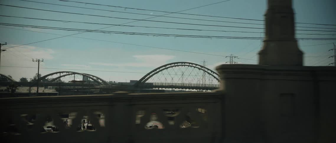 A truck drives by a stone gate that has several arched bridges behind it