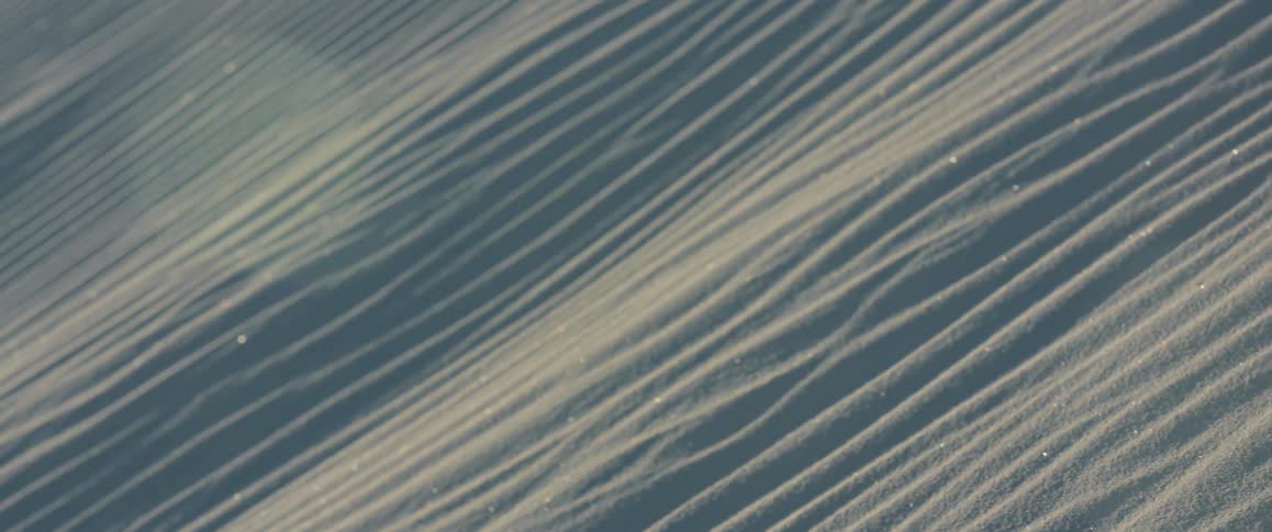 Stretches of an unbroken greyish white sand dune stretch out with ridges and particles glistening in the sun