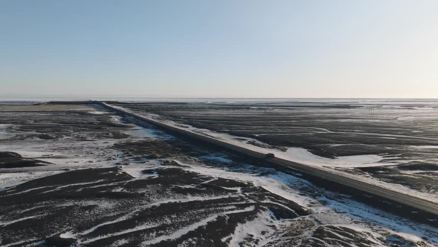 Lone vehicle drives along a highway passing icy fields on a winter day