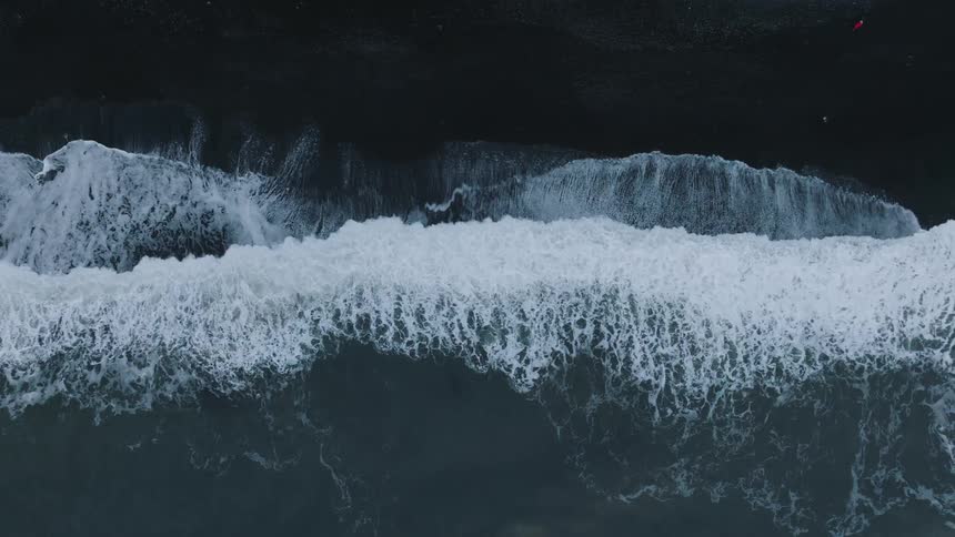 Birds eye view of waves crashing onto shoreline of black sand beach