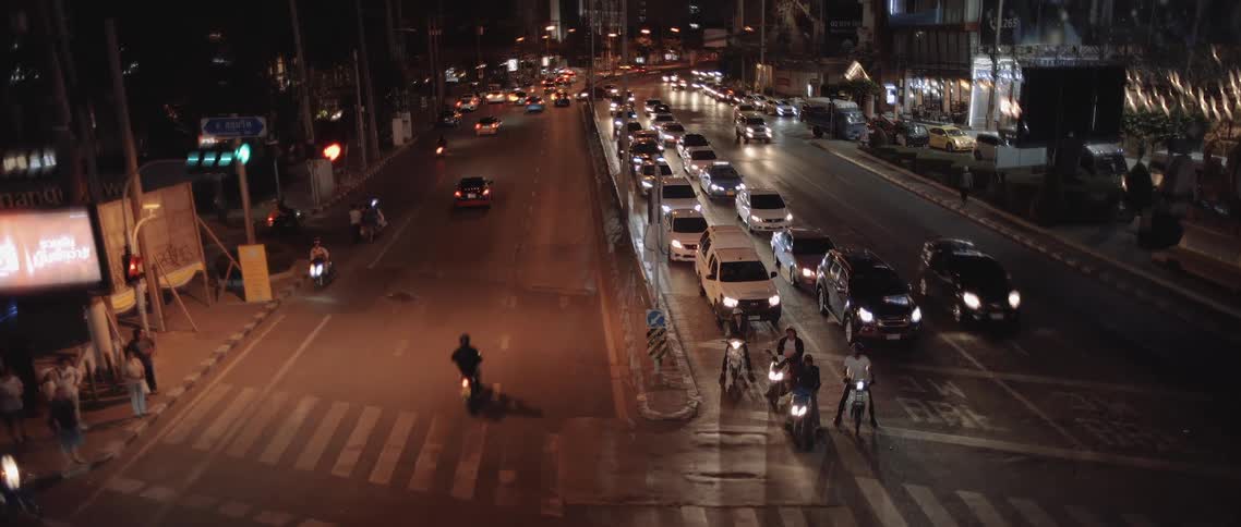 A busy city intersection filled with cars motorcycles and pedestrians under streetlights and traffic signals