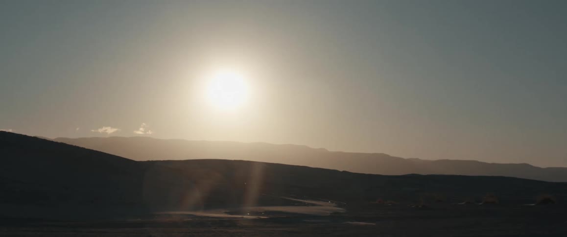 A sun low in the sky casting a soft glow over a landscape of rolling hills and distant mountains