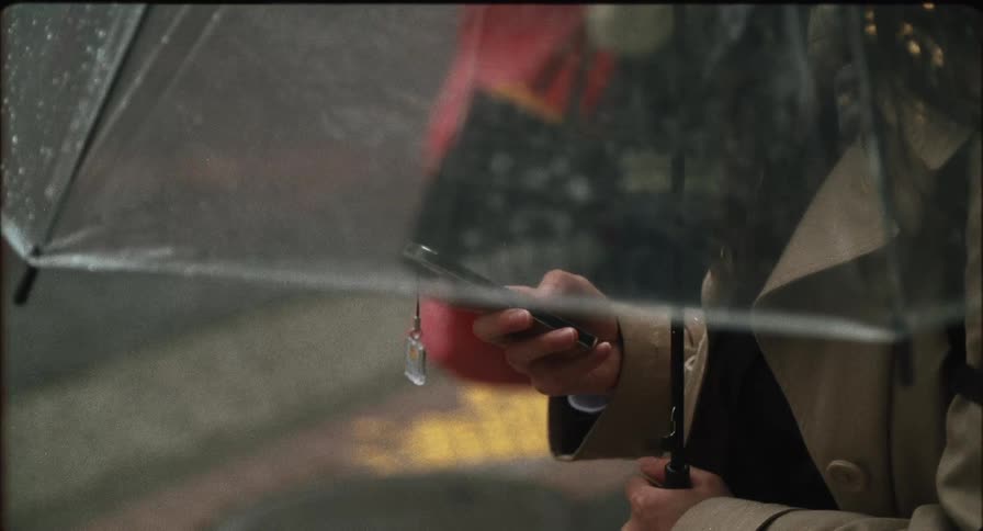 Female holding a clear umbrella in the rain scrolling on a cell phone