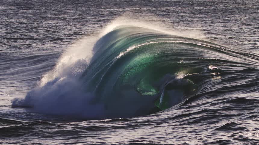 A large blueish green wave crashing in on itself and a beautiful mist of spray outlines the wave
