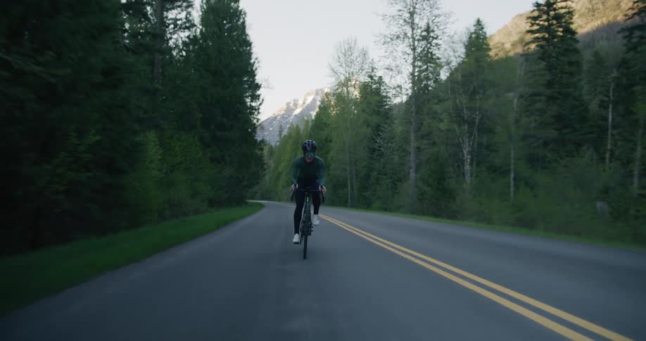 Cyclist riding on road surrounded by trees through the mountains