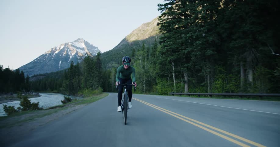 Cyclist riding on road across the forest alongside a river