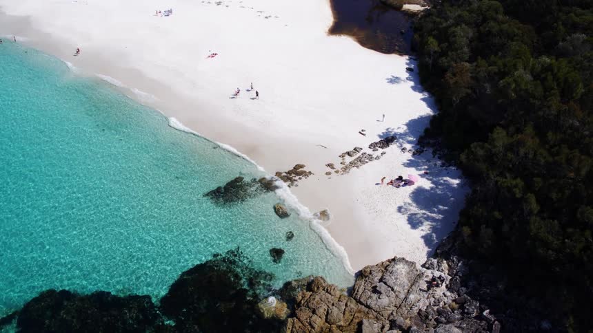 An aerial view showcases a pristine white sand beach fringed by turquoise waters and lush coastal vegetation
