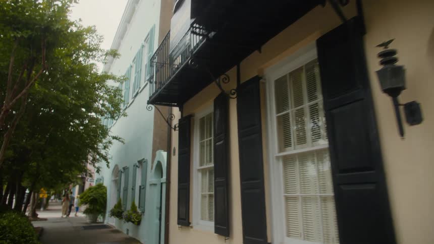 A historic building featuring a black wroughtiron balcony whiteframed windows with black shutters and a white arched doorway with a black door all set against a backdrop of pastelcolored facades