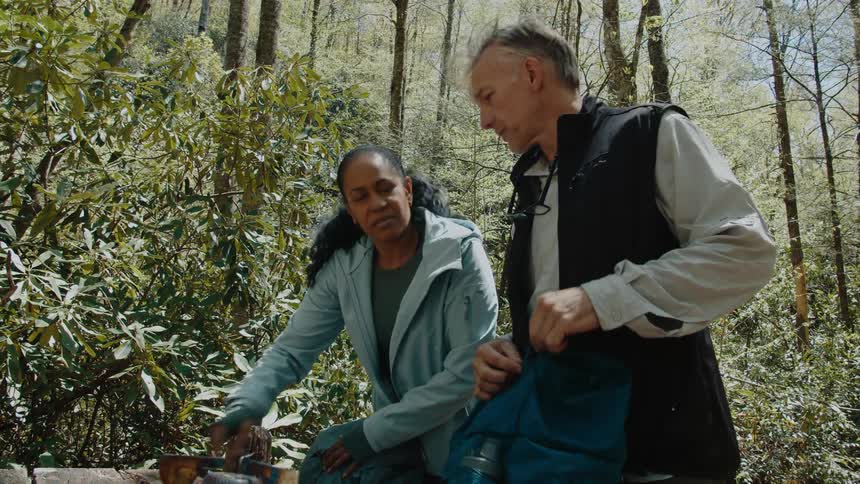 A woman shows a man her camera by the forest